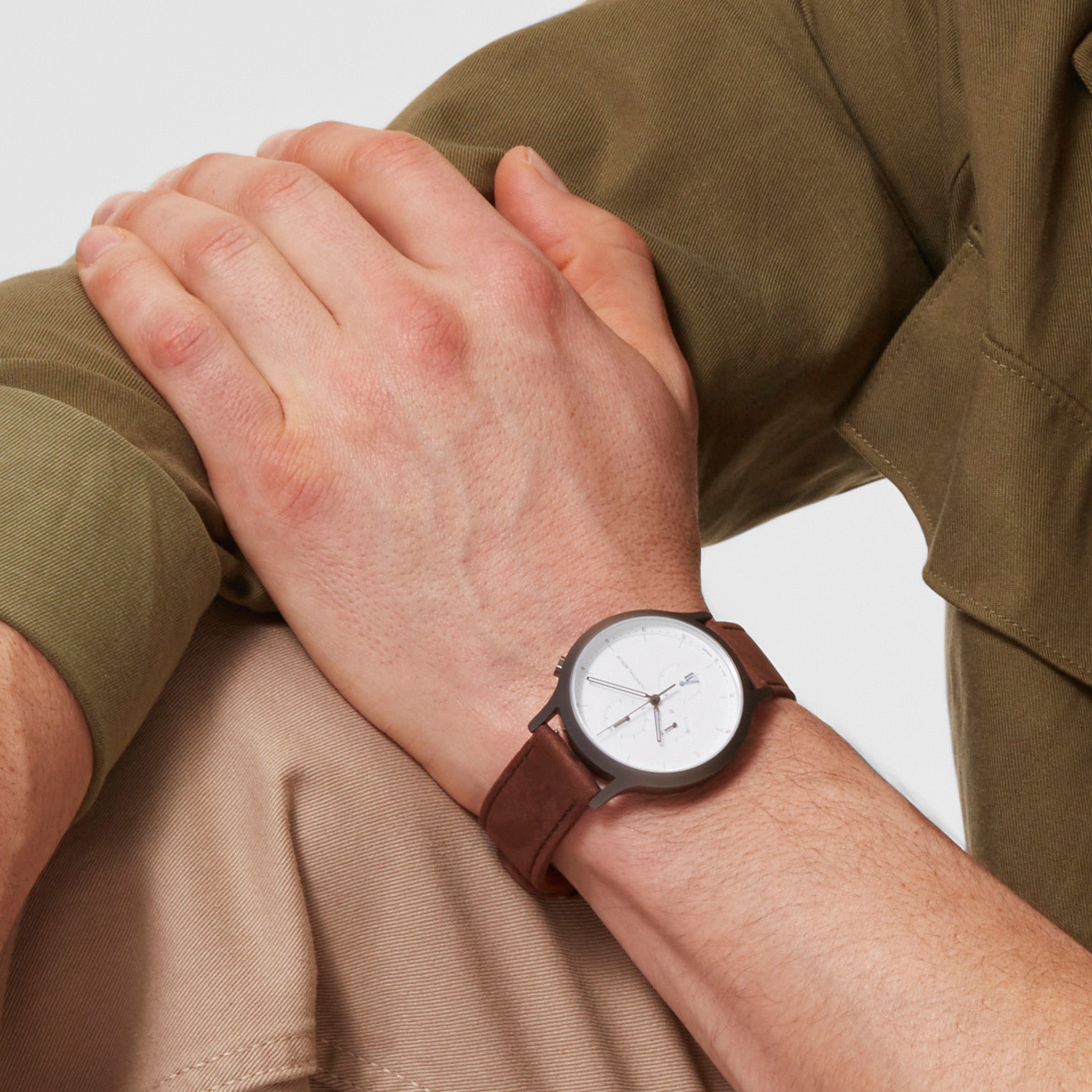 Minimalist wristwatch with white dial and brown leather strap on man's wrist