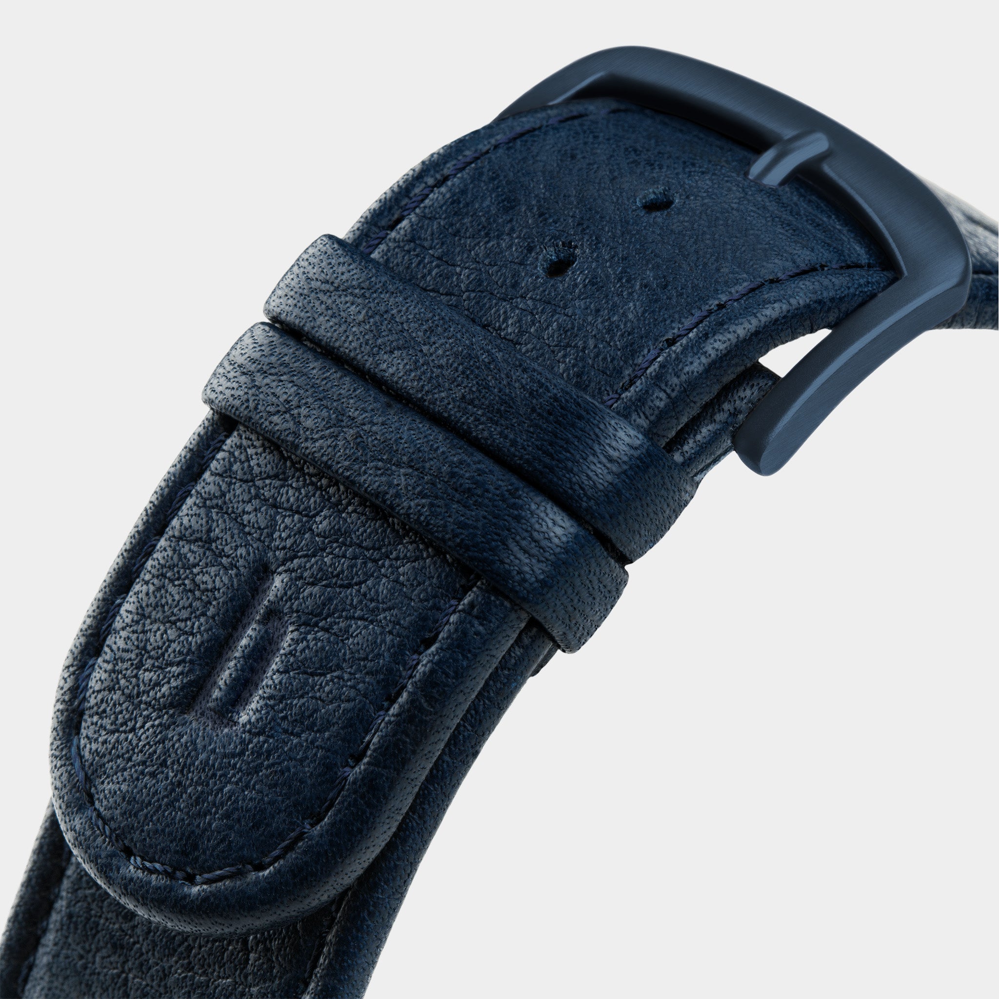 Close-up of a textured dark blue leather watch strap with matte black buckle