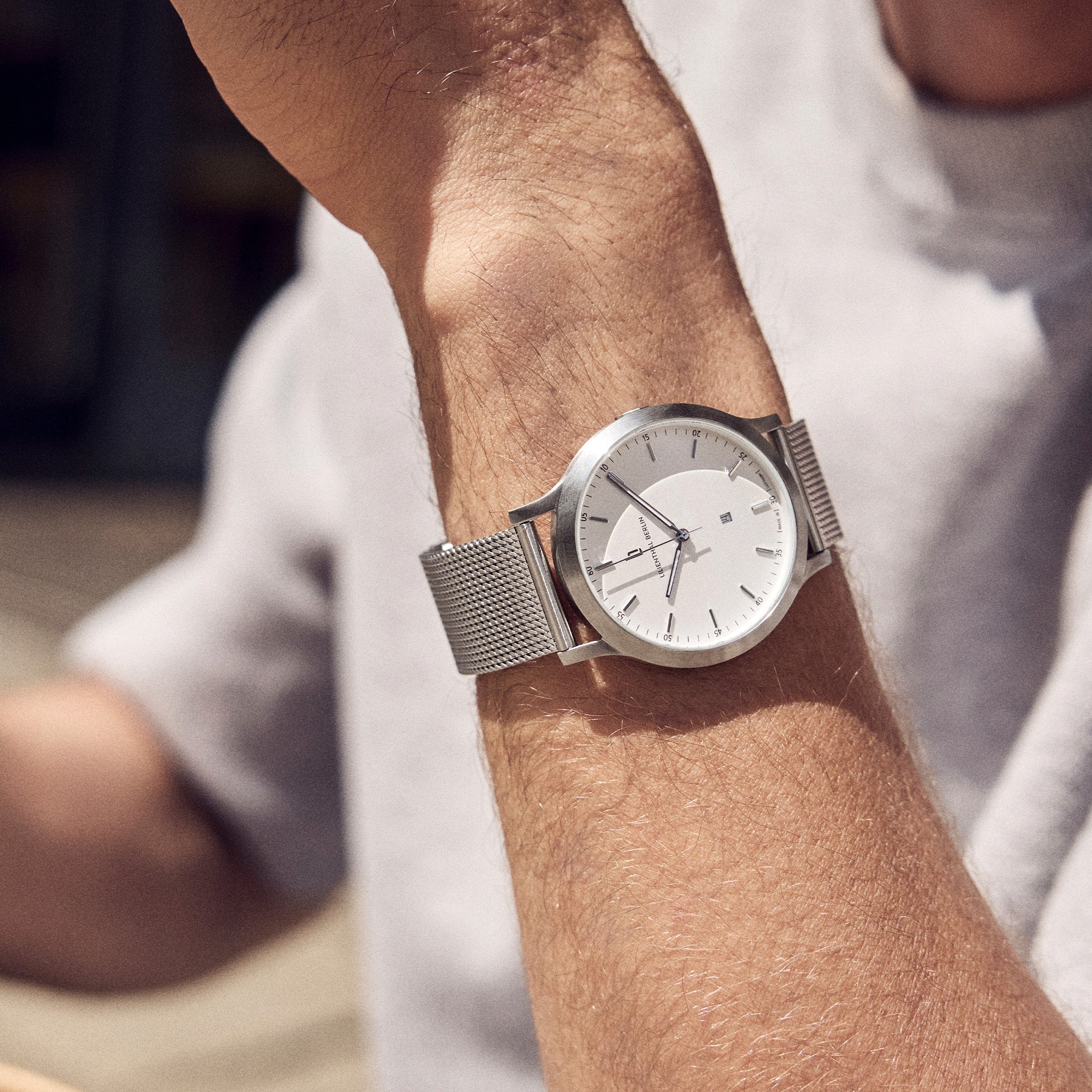 Minimalist silver mesh strap watch with white dial on wrist, modern outdoor style