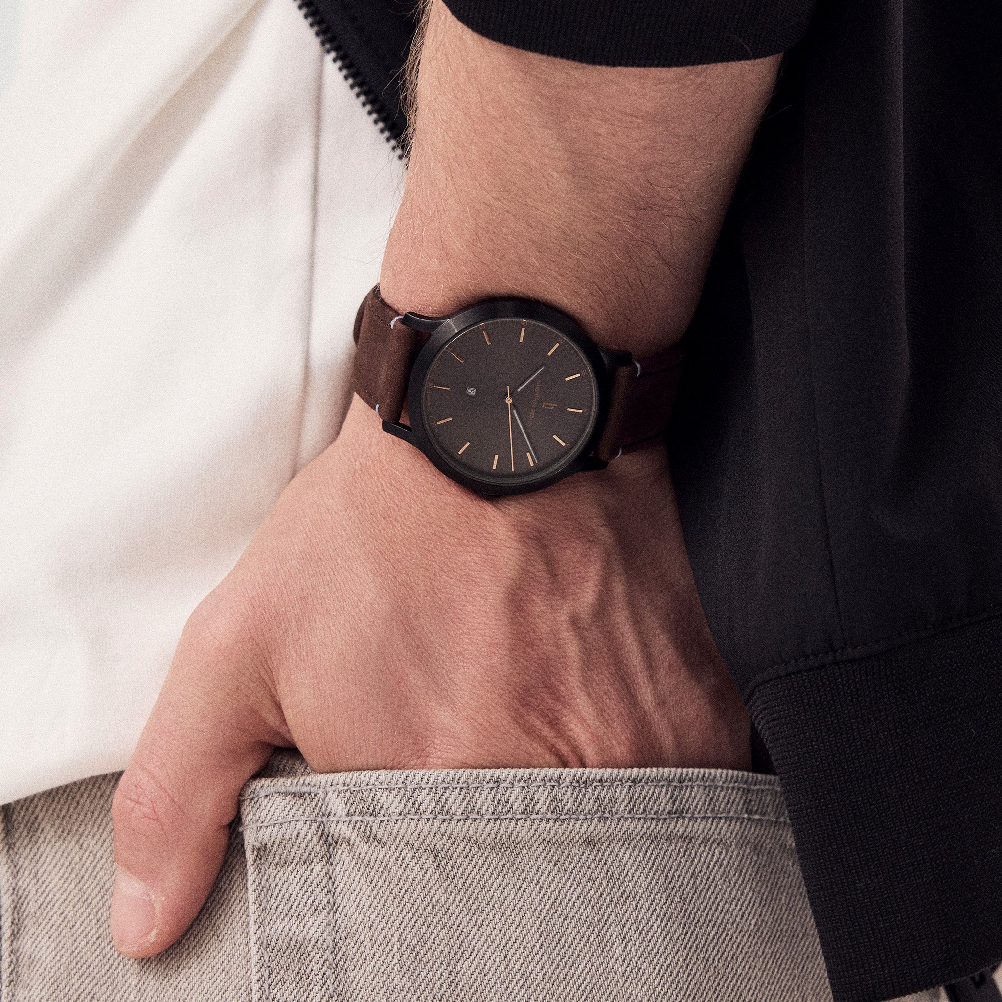 Minimalist black wristwatch with brown leather strap on man's wrist, casual outfit