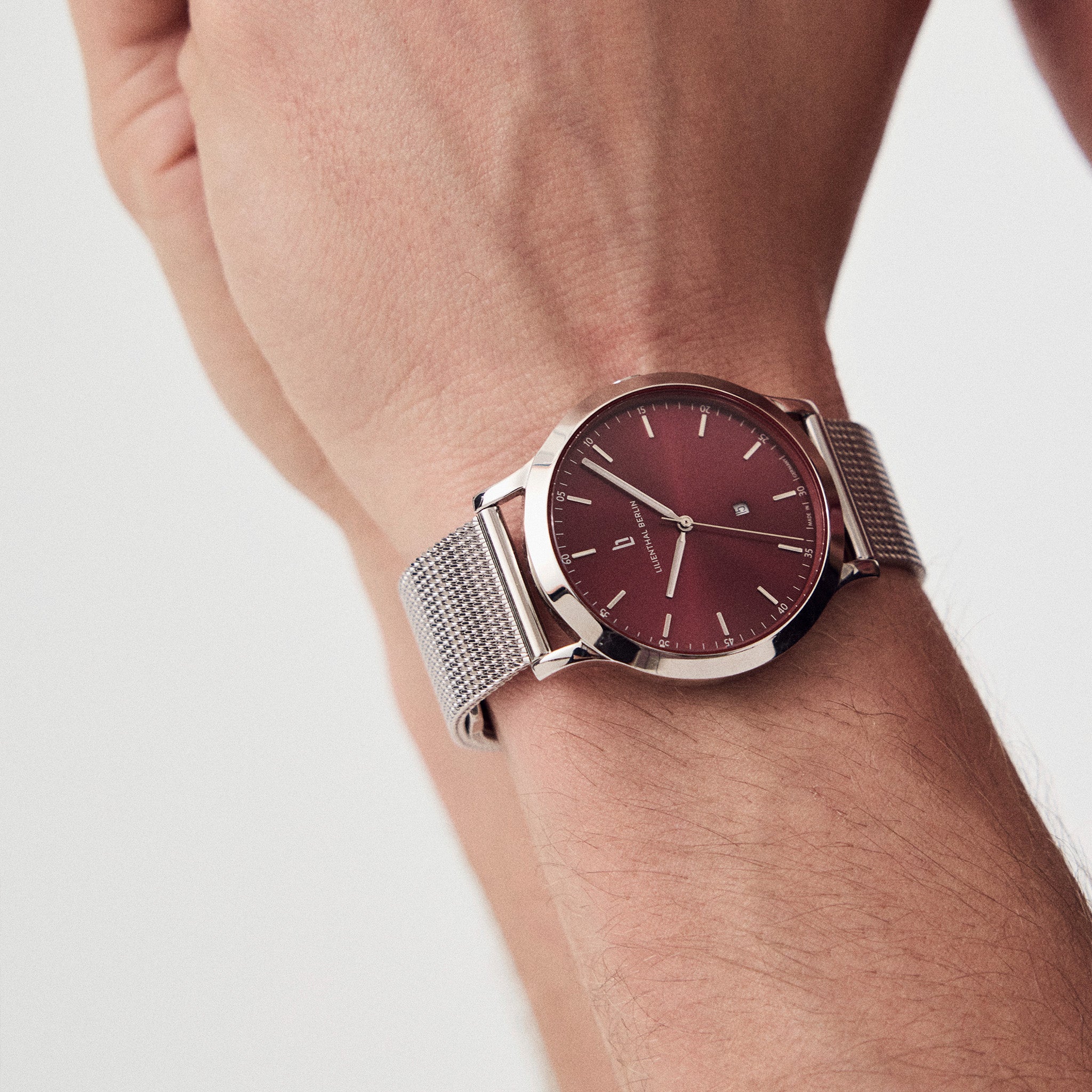 Minimalist silver mesh watch with burgundy dial on wrist, modern and stylish accessory