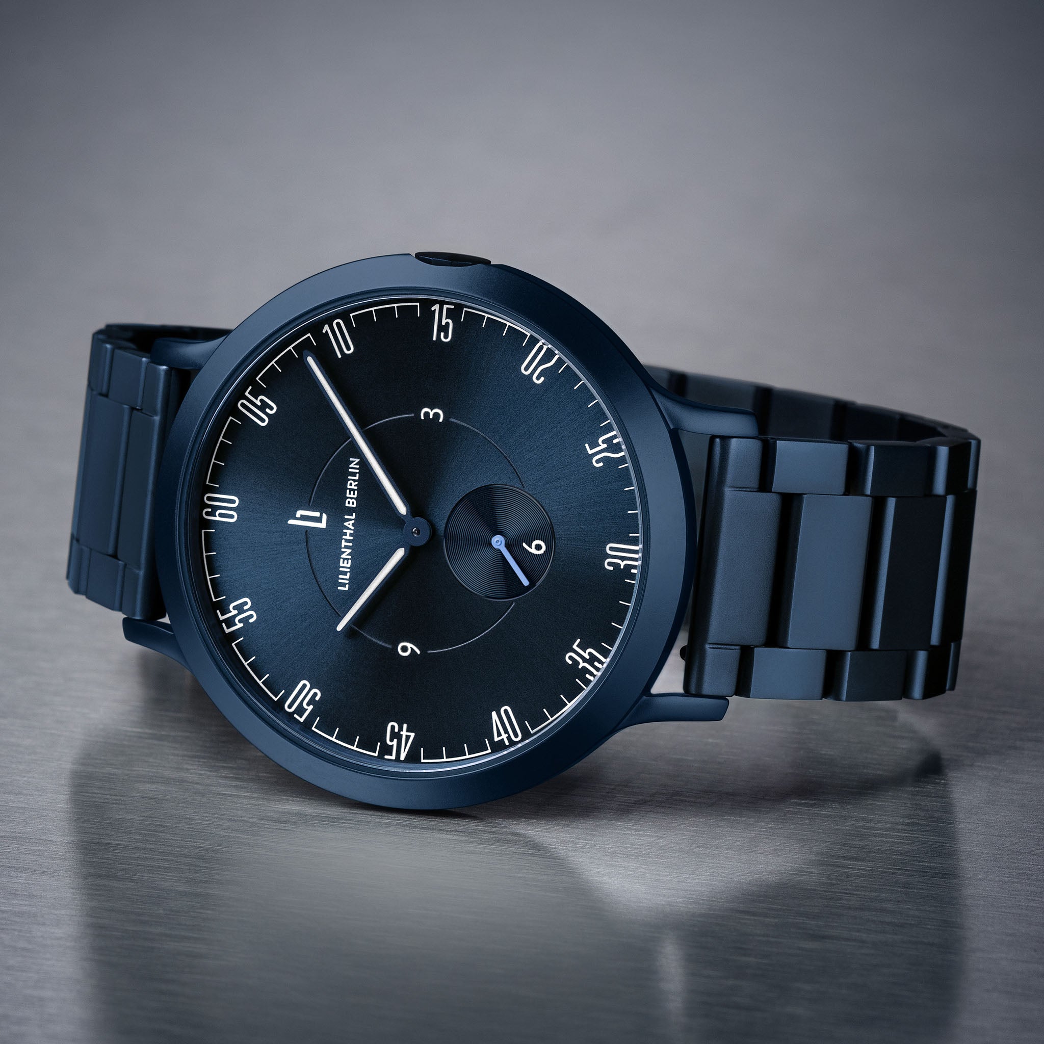 Matte black minimalist wristwatch with metal link strap and modern dial on grey surface.