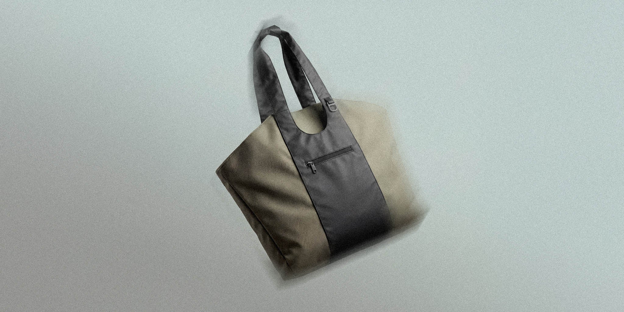 Modern two-tone tote bag with black center panel and zipper pocket on neutral background