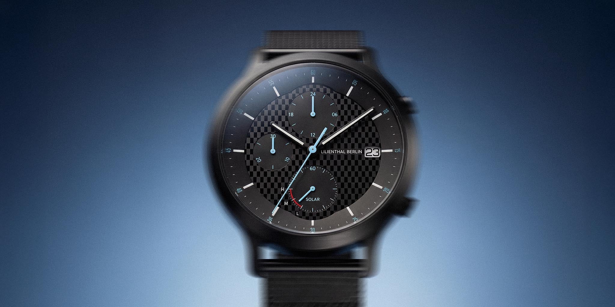 Black chronograph solar-powered wristwatch with checkered dial and mesh strap on gradient background