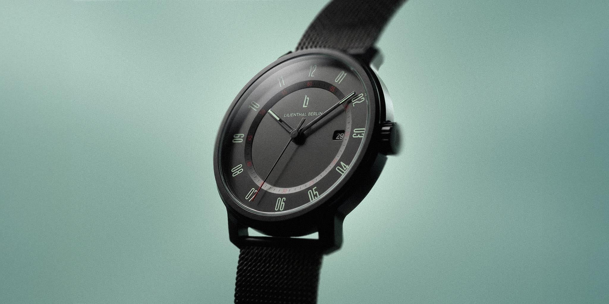 Minimalist black wristwatch with mint green dial accents and mesh strap on mint background