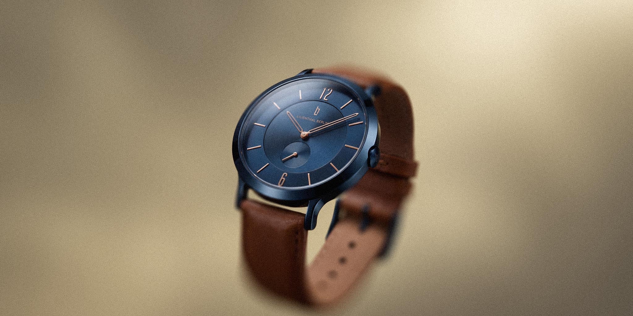 Classic blue watch with rose gold details and brown leather strap on neutral background