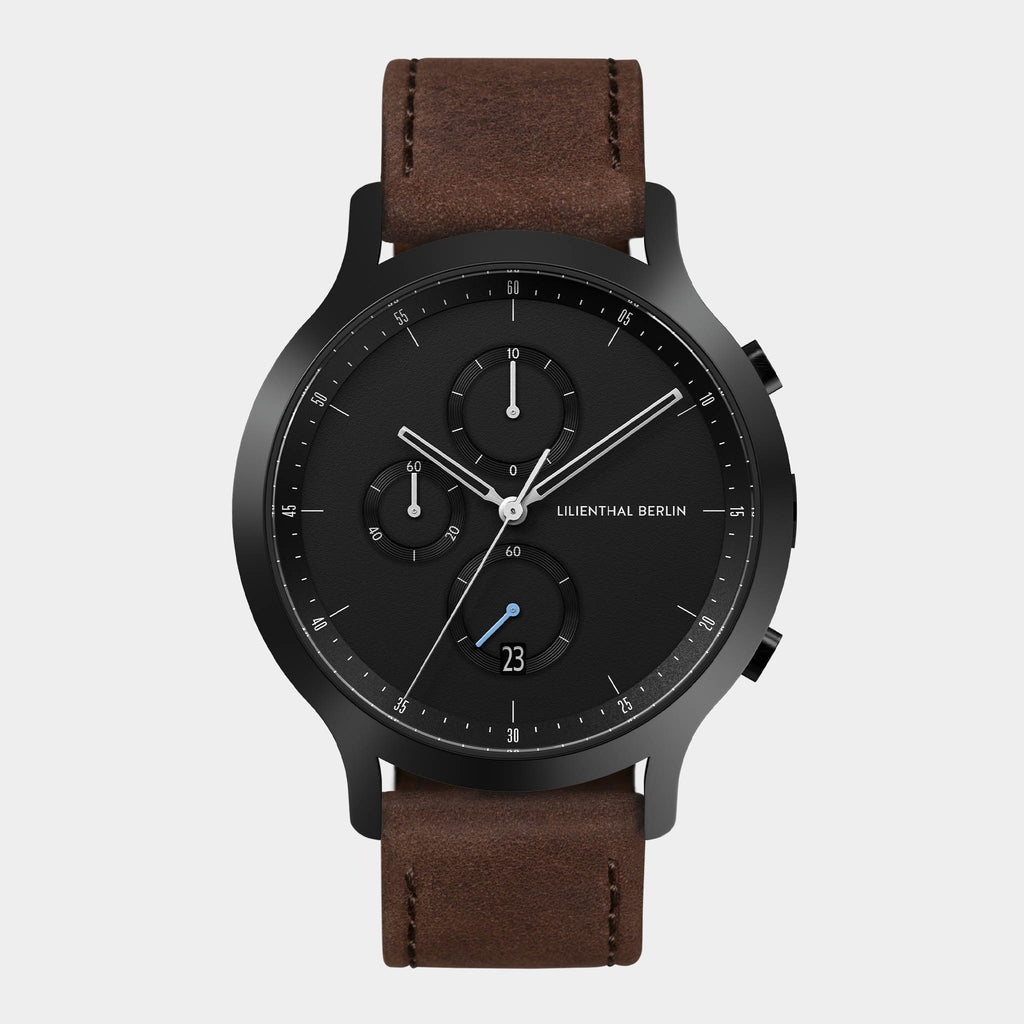 Black chronograph watch with brown leather strap and date display on white background
