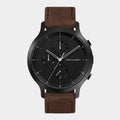 Black chronograph watch with brown leather strap and date display on white background