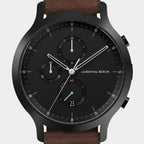 Black chronograph watch with subdials, date display, and brown leather strap
