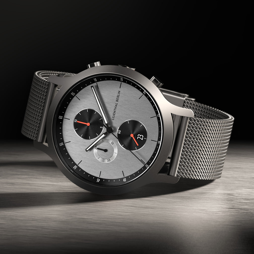 Modern chronograph watch with mesh strap, silver dial, black subdials, and red accents