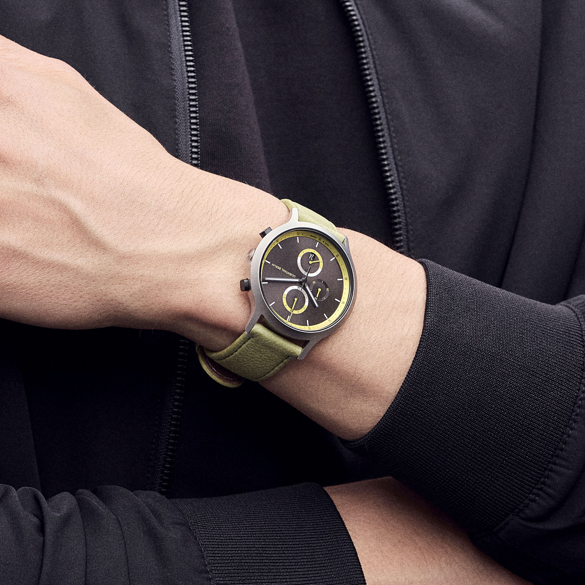 Modern wristwatch with green strap and black-yellow dial on person's wrist, close-up