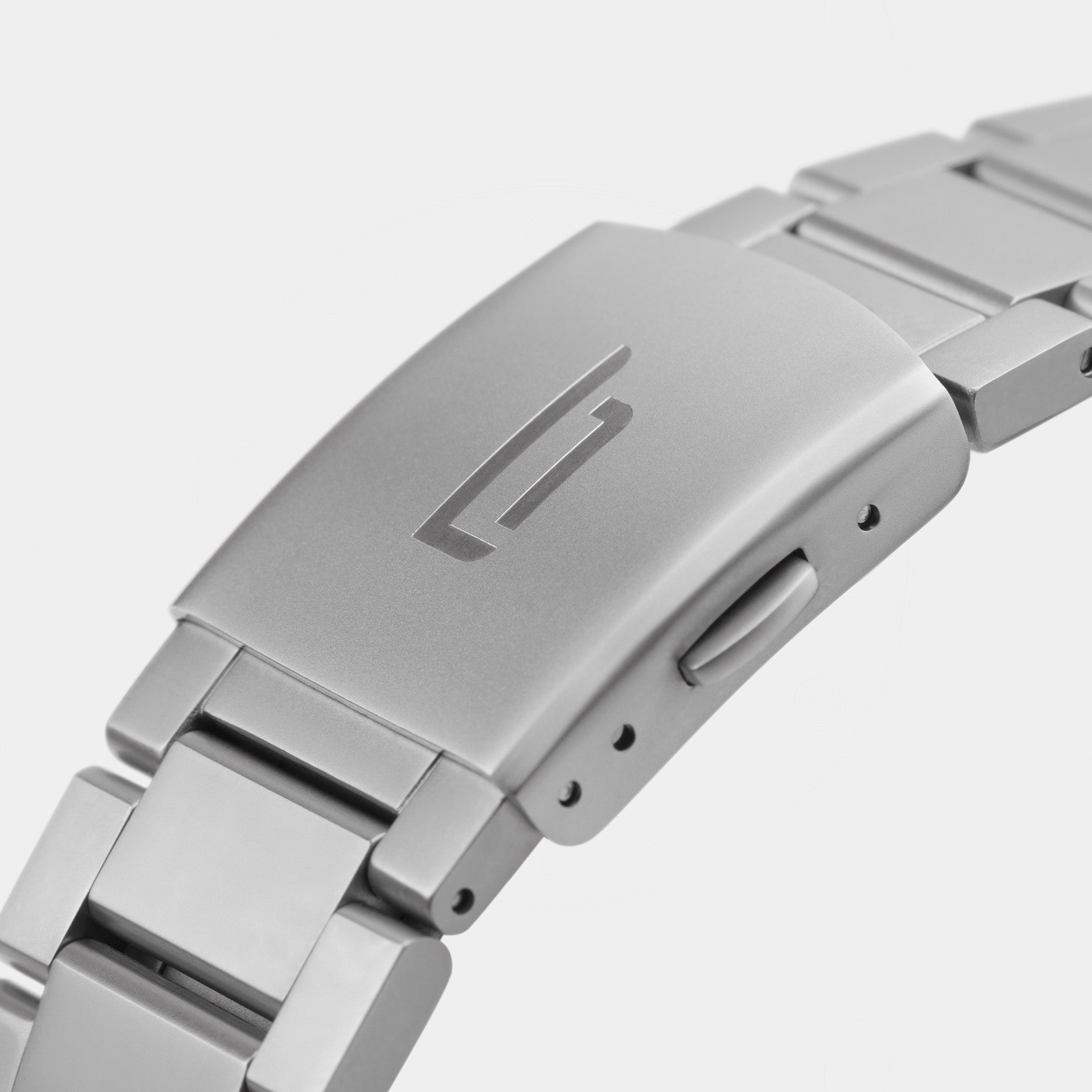 Close-up of a stainless steel watch bracelet clasp with engraved logo and brushed metal finish
