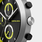 Close-up of a modern chronograph watch with yellow accents and stainless steel case.