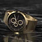 Gold chronograph watch with mesh strap and black dial on marble surface