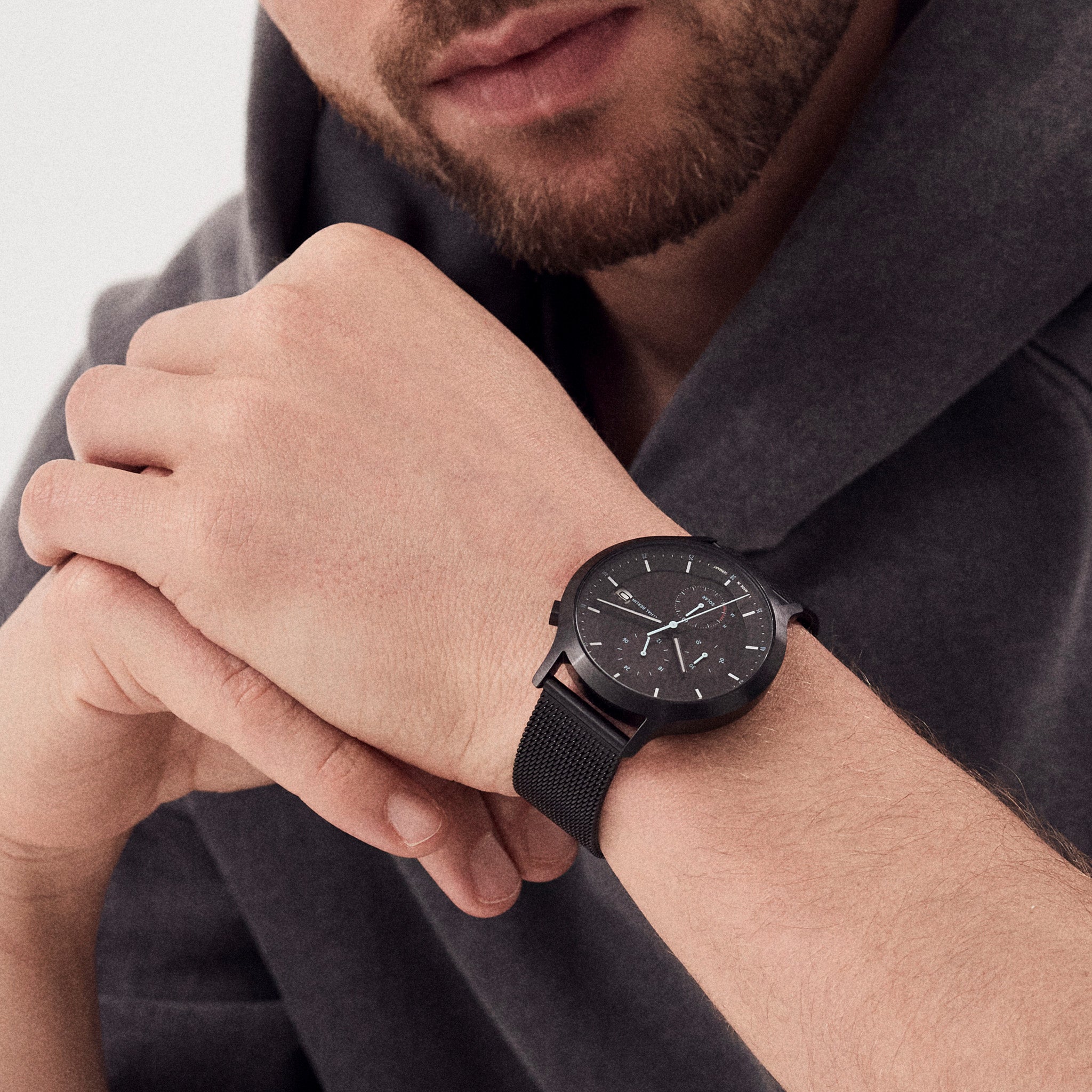 Man wearing minimalist black wristwatch with mesh band on left wrist