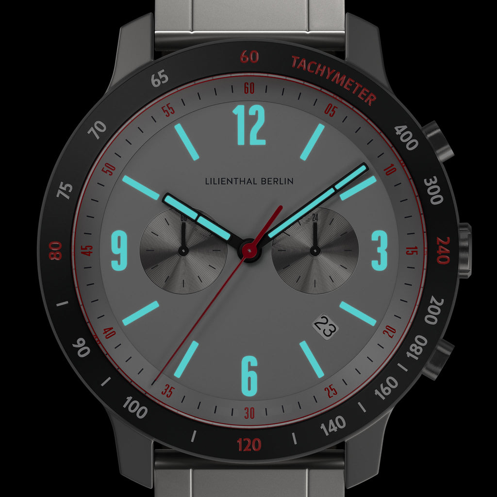 Modern chronograph watch with gray dial, luminous blue markers, and tachymeter bezel.