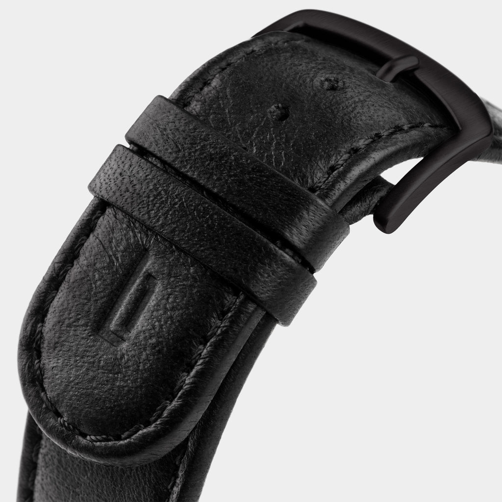 Close-up of a black leather watch strap with matte black buckle and stitched detailing