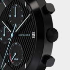 Close-up of a black chronograph watch with a carbon fiber dial, subdials, and date display.