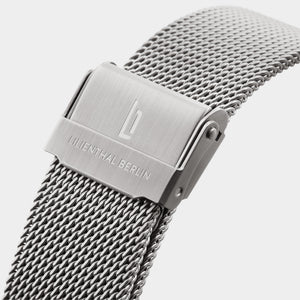 Close-up of stainless steel mesh watch strap with engraved clasp on white background